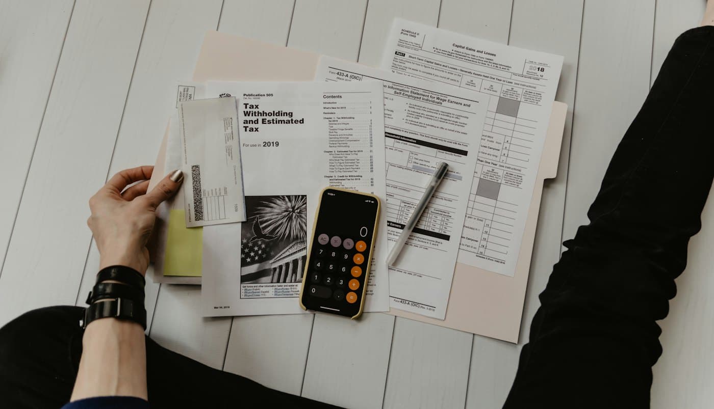 Tax forms, a calculator and a phone laid out on a table