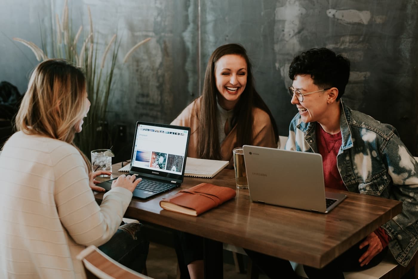 Three colleagues laughing together around a table with laptops